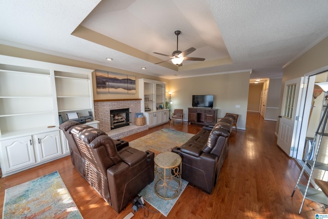 living room with hardwood / wood-style flooring, crown molding, a raised ceiling, and a brick fireplace