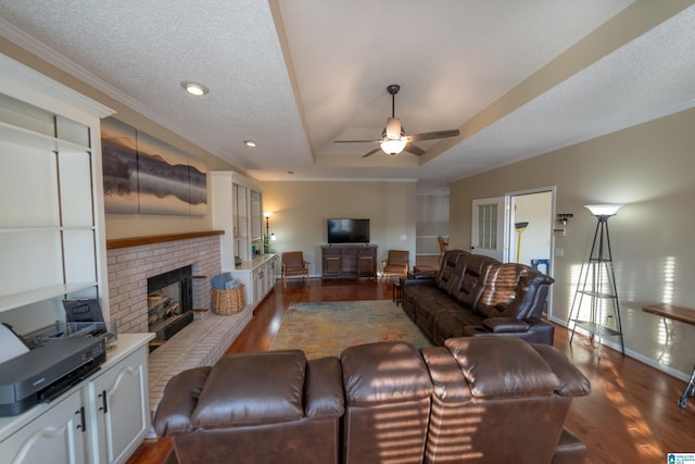 living room with a fireplace, dark hardwood / wood-style flooring, ceiling fan, a raised ceiling, and a textured ceiling