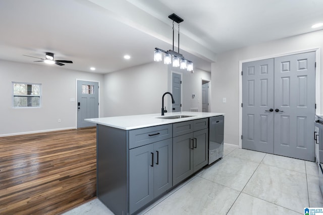 kitchen with sink, hanging light fixtures, stainless steel dishwasher, gray cabinets, and an island with sink