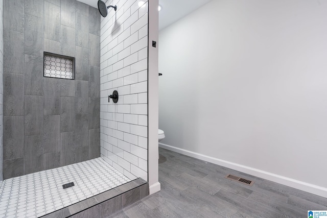 bathroom with wood-type flooring, tiled shower, and toilet