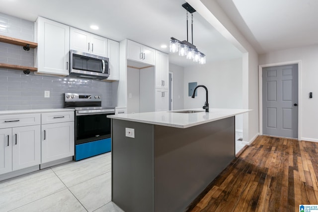 kitchen with sink, hanging light fixtures, a center island with sink, stainless steel appliances, and white cabinets