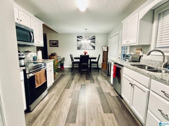 kitchen with sink, hanging light fixtures, stainless steel appliances, light stone countertops, and white cabinets