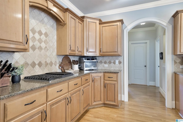 kitchen with stainless steel gas cooktop, crown molding, light hardwood / wood-style flooring, dark stone counters, and decorative backsplash