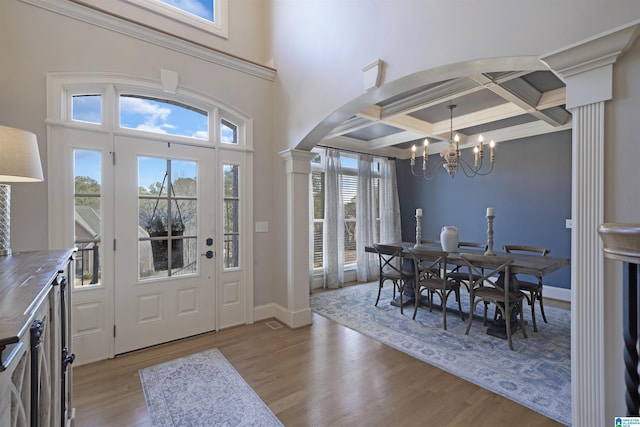 entrance foyer with ornate columns, a healthy amount of sunlight, coffered ceiling, and light hardwood / wood-style flooring