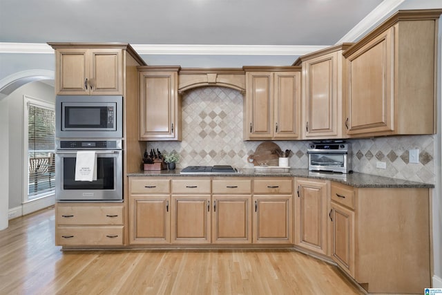 kitchen featuring tasteful backsplash, light wood-type flooring, ornamental molding, appliances with stainless steel finishes, and dark stone counters