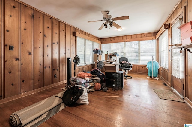 interior space featuring wood-type flooring, wooden walls, ceiling fan, and plenty of natural light