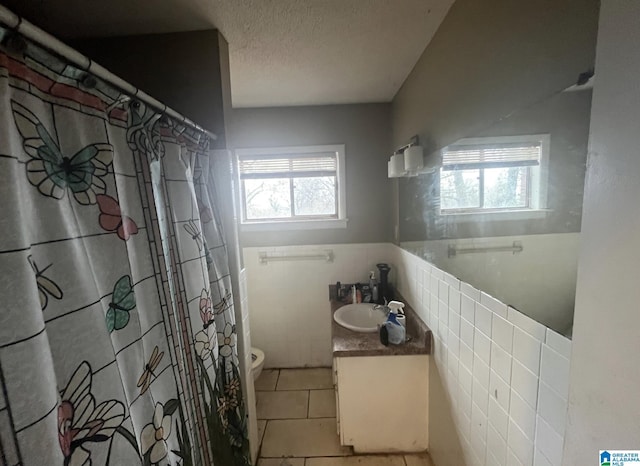 bathroom with toilet, tile walls, a textured ceiling, vanity, and tile patterned flooring