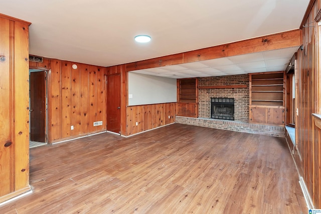 unfurnished living room with a fireplace, light hardwood / wood-style floors, built in features, and wood walls