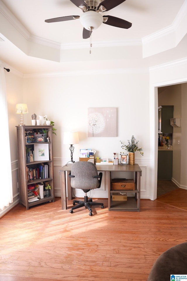 office featuring a tray ceiling, ornamental molding, light hardwood / wood-style floors, and ceiling fan