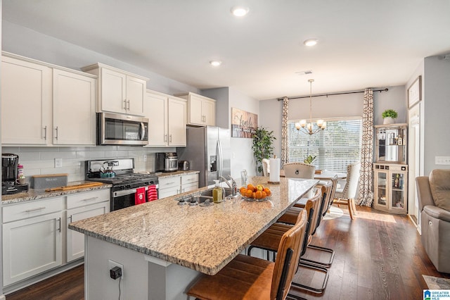 kitchen featuring light stone counters, decorative light fixtures, stainless steel appliances, and an island with sink