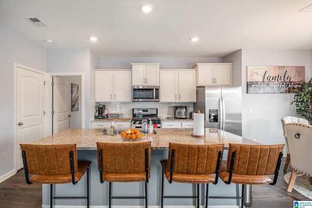 kitchen with white cabinetry, appliances with stainless steel finishes, a kitchen bar, and a kitchen island with sink