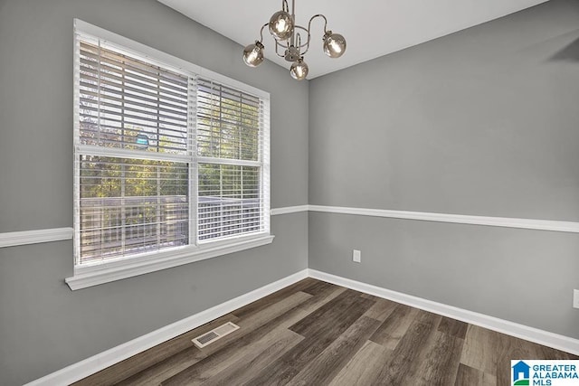 empty room with a notable chandelier and dark hardwood / wood-style flooring