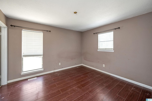 spare room featuring a textured ceiling and dark hardwood / wood-style flooring