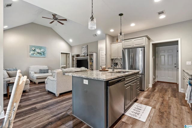 kitchen featuring sink, gray cabinets, appliances with stainless steel finishes, light stone counters, and a center island with sink