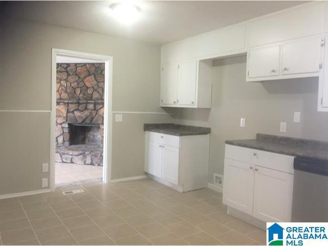 2838 Micmac Dr, Birmingham, AL 35215 - kitchen with stainless steel dishwasher, dark countertops, a fireplace, and white cabinetry