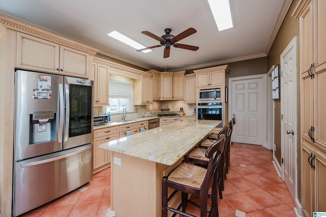 kitchen with a kitchen island, sink, a kitchen bar, light stone counters, and stainless steel appliances