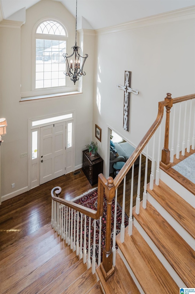 foyer featuring crown molding, wood-type flooring, high vaulted ceiling, and a chandelier