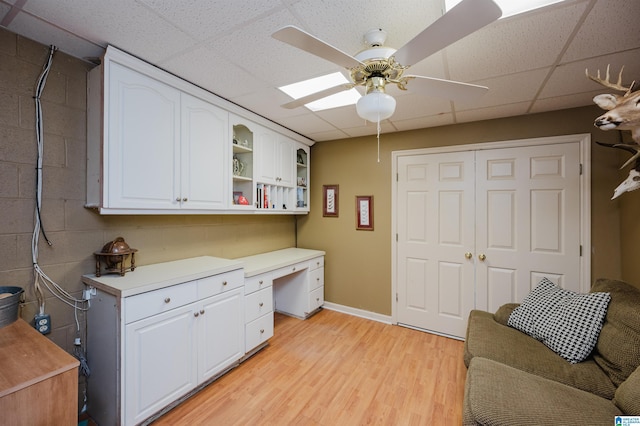 interior space with ceiling fan, white cabinetry, built in desk, light hardwood / wood-style floors, and a drop ceiling