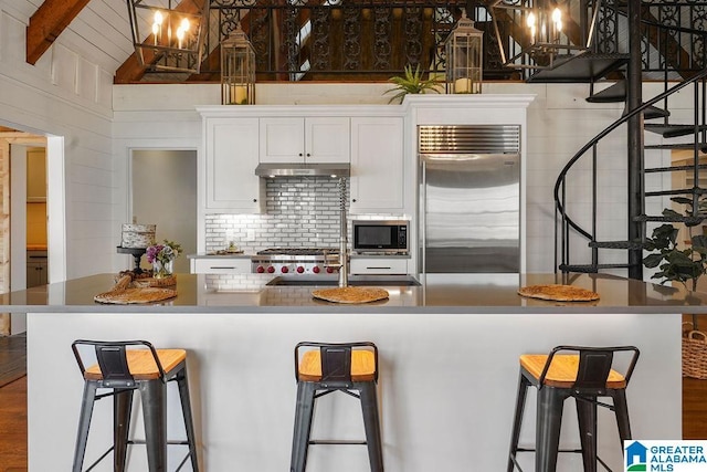 kitchen featuring a breakfast bar area, vaulted ceiling with beams, built in appliances, white cabinets, and backsplash