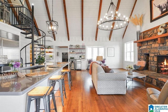 living room featuring a notable chandelier, beam ceiling, a fireplace, and wood-type flooring