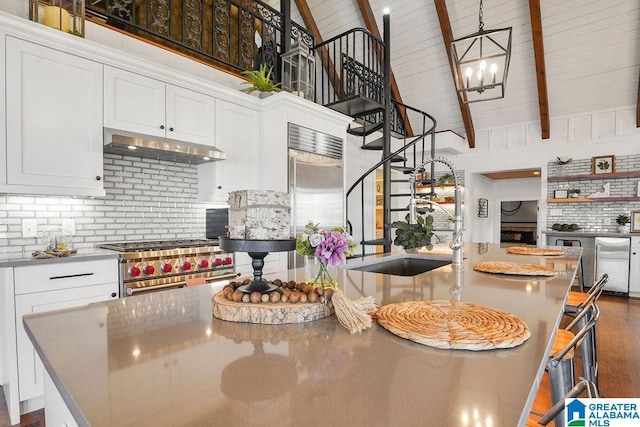 kitchen with white cabinetry, high quality appliances, beam ceiling, and an island with sink