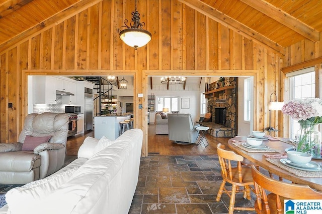 living room with a fireplace, wood walls, beamed ceiling, wooden ceiling, and an inviting chandelier