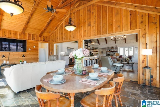 dining space featuring ceiling fan with notable chandelier, wooden walls, wooden ceiling, and beamed ceiling