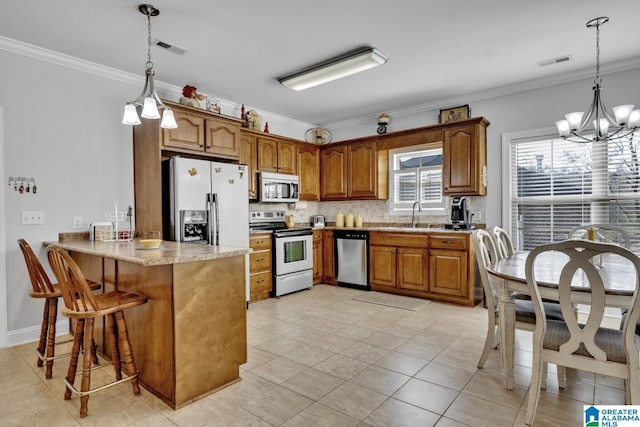 kitchen with stainless steel appliances, brown cabinetry, ornamental molding, a sink, and a peninsula