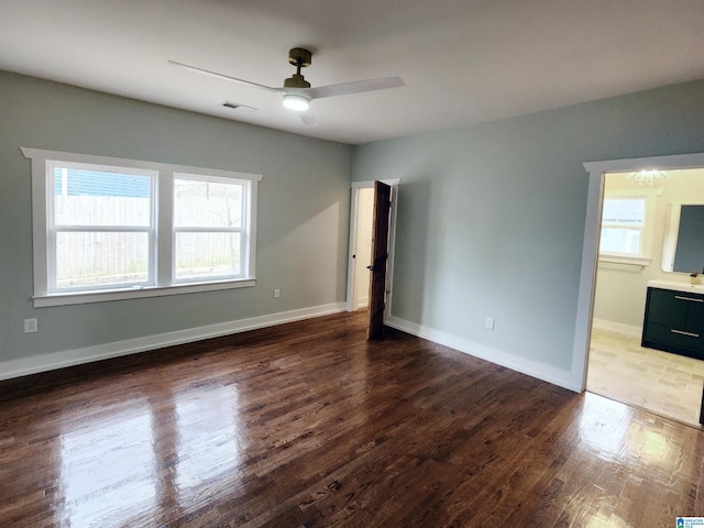 unfurnished bedroom with dark wood-type flooring, ceiling fan, ensuite bathroom, and multiple windows