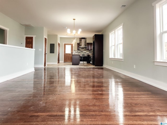 unfurnished living room featuring a wealth of natural light, electric panel, dark hardwood / wood-style floors, and a chandelier