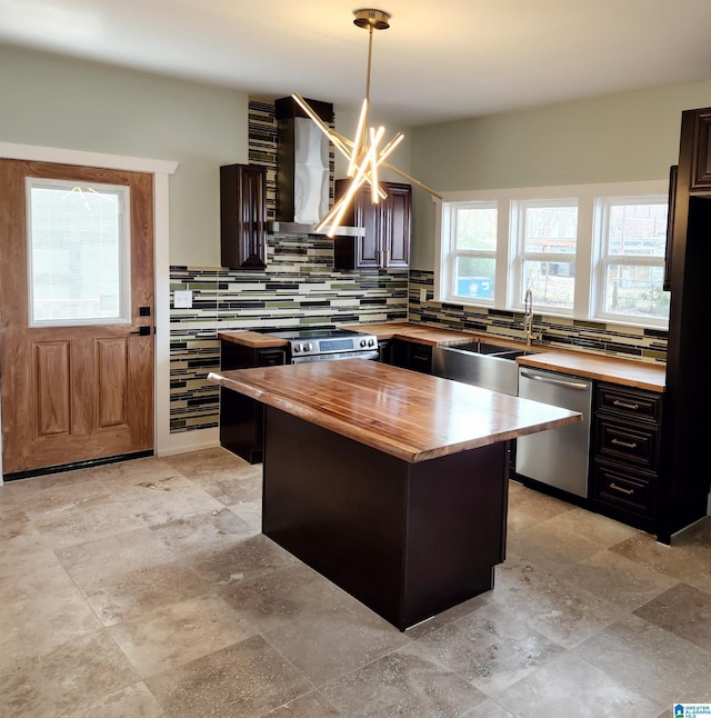 kitchen with butcher block counters, decorative light fixtures, dishwasher, a kitchen island, and wall chimney range hood