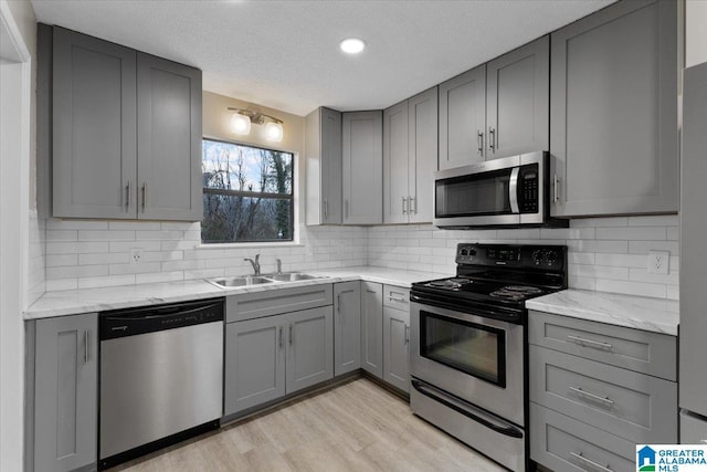 kitchen with sink, gray cabinetry, light stone counters, stainless steel appliances, and light hardwood / wood-style flooring