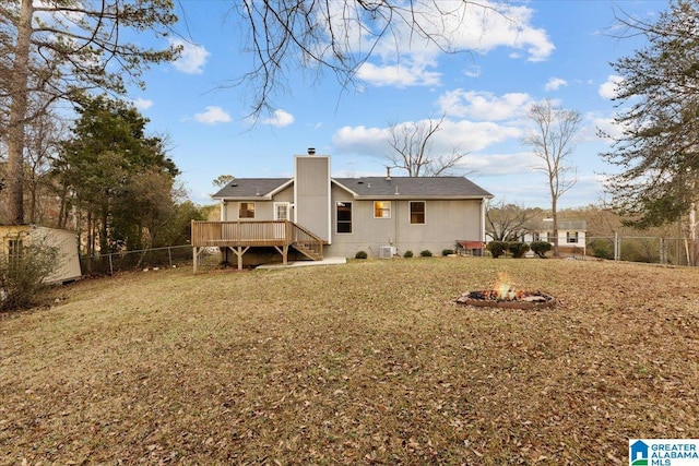 back of property featuring a wooden deck, a fire pit, and a lawn