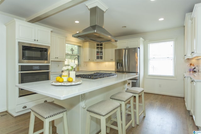 kitchen with stainless steel appliances, island range hood, white cabinets, and backsplash