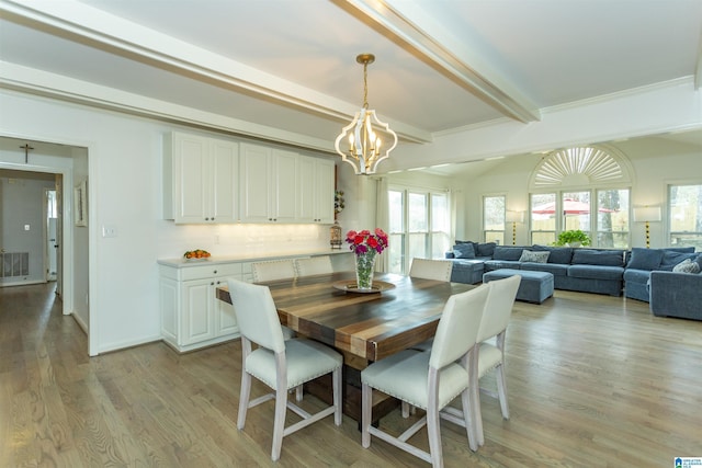 dining space featuring a chandelier, beam ceiling, and light hardwood / wood-style floors