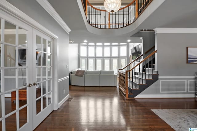 entryway featuring dark wood-type flooring, french doors, crown molding, a chandelier, and a towering ceiling