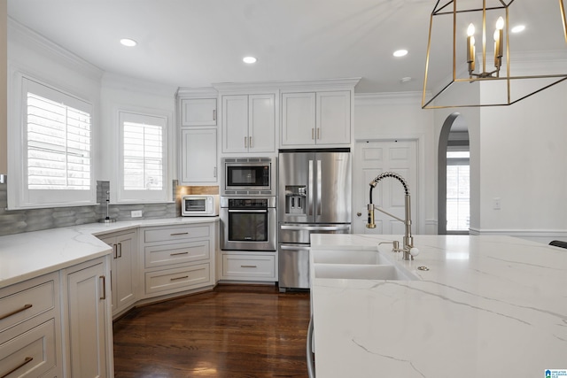 kitchen featuring sink, hanging light fixtures, stainless steel appliances, crown molding, and light stone countertops