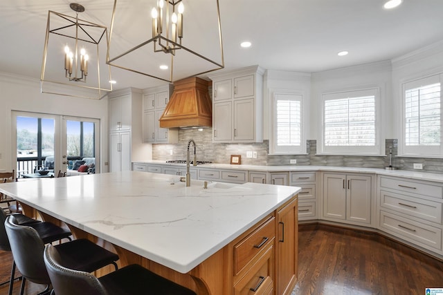 kitchen with a kitchen island with sink, decorative light fixtures, white cabinets, and premium range hood