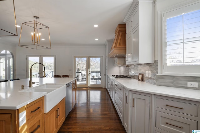 kitchen with french doors, premium range hood, stainless steel appliances, light stone countertops, and a kitchen island with sink