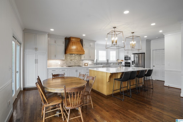 kitchen featuring appliances with stainless steel finishes, an island with sink, a kitchen breakfast bar, custom exhaust hood, and hanging light fixtures