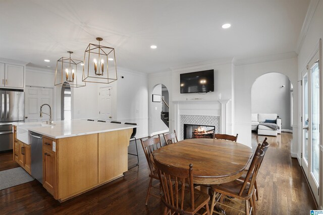 interior space featuring sink, appliances with stainless steel finishes, a fireplace, a kitchen island with sink, and white cabinets