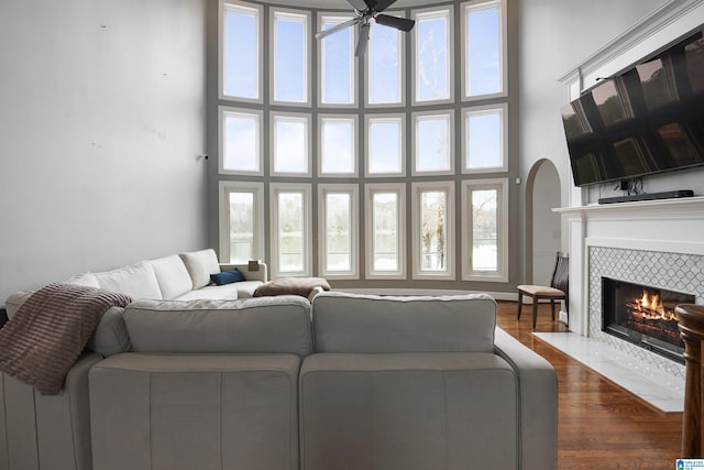 living room with ceiling fan, wood-type flooring, a tiled fireplace, and a high ceiling