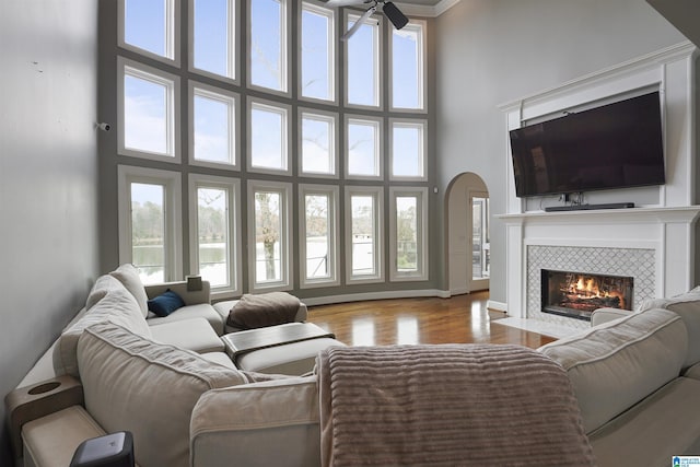 living room with a tiled fireplace, a high ceiling, ceiling fan, and light hardwood / wood-style flooring