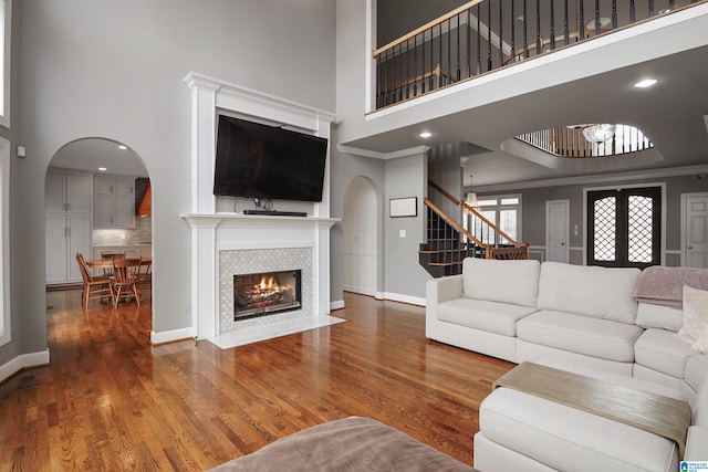 living room featuring a high ceiling, wood-type flooring, a tiled fireplace, and crown molding