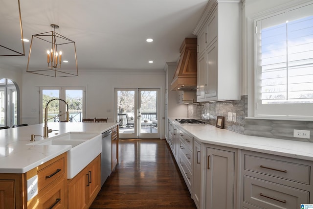 kitchen with french doors, light stone counters, decorative light fixtures, appliances with stainless steel finishes, and custom range hood