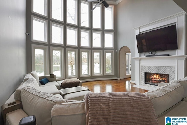 living room with a high ceiling, a tile fireplace, ceiling fan, and light hardwood / wood-style flooring