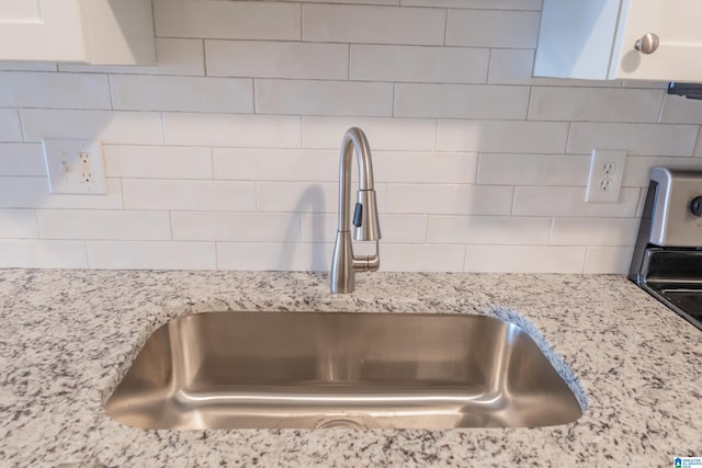 room details with white cabinetry, sink, backsplash, and light stone counters