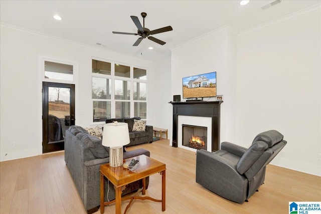 living area featuring crown molding, visible vents, light wood-type flooring, and a warm lit fireplace