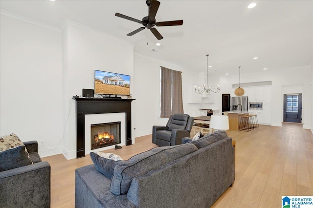 living room with ornamental molding, ceiling fan with notable chandelier, and light hardwood / wood-style flooring