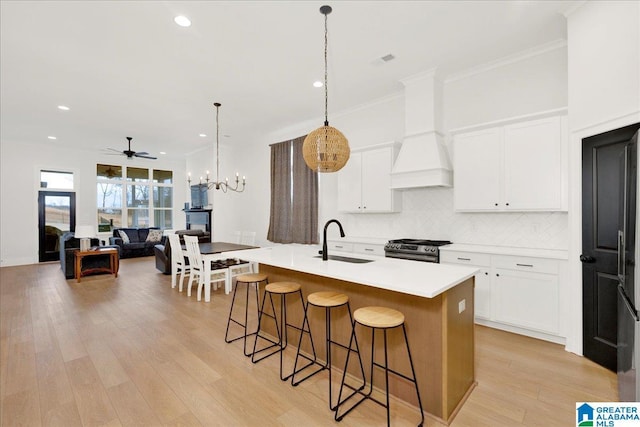 kitchen featuring sink, premium range hood, a kitchen island with sink, white cabinetry, and stainless steel range with gas stovetop